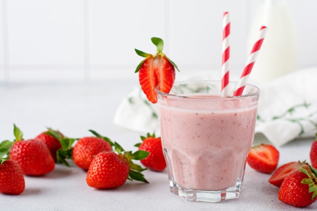 Erdbeersmoothie oder Milchshake mit Beeren und Haferflocken im Glas auf grauem oder weißem Betonhintergrund. Vegetarisches gesundes Getränk. Nahaufnahme. Selektiver Fokus