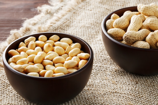 Erdnüsse in der Schale und geschälte Nahaufnahme in Tassen, geröstete Erdnüsse in der Schale und geschält gegen ein braunes Tuch