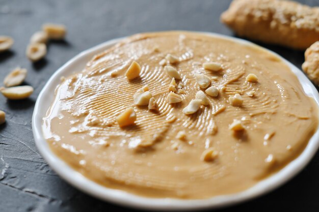 Foto erdnussbutter auf einem teller mit gesalzenen erdnüssen, paleo-diät und keto-diät, traditionelle zutat für leckeres frühstück, dunkler hintergrund, fettquelle, selektiver fokus