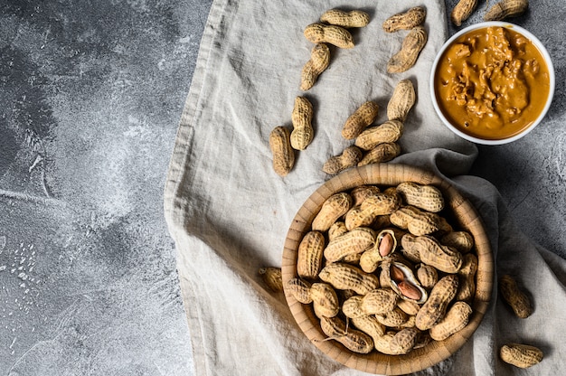 Erdnussbutter in einer Schüssel, rohe Erdnüsse. Vegetarisches Essen. Grauer Hintergrund. Draufsicht. Platz für Text