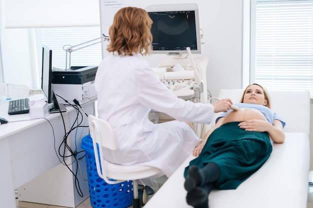 Erfahrene Ärztin, die Ultraschall des Bauches einer schwangeren Frau in einer medizinischen Klinik durchführt. Konzept der glücklichen und gesunden Geburt.