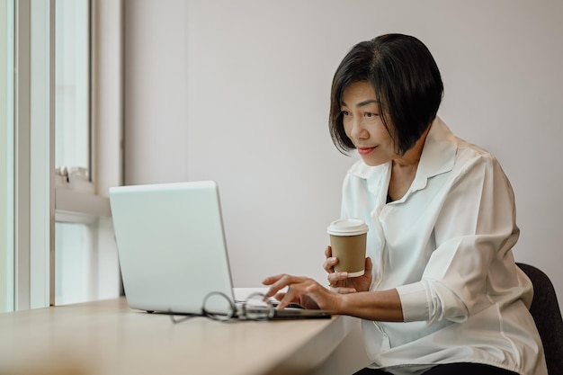 Erfahrene Geschäftsfrau, die auf einem Laptop tastet, online arbeitet und ein Projekt am Schreibtisch plant