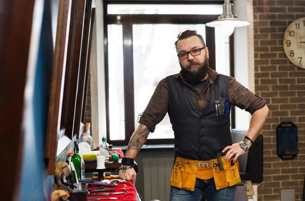 Foto erfahrener bärtiger friseur am arbeitsplatz im friseursalon. professioneller stilvoller friseur wartet auf kunden im friseursalon