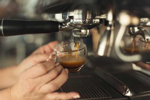 Erfahrener Barmann, der Espresso in einer modernen Kaffeemaschine zubereitet. Nahaufnahme der weiblichen Hand, die verspannendes Getränk zubereitet. Kleines Unternehmen und professionelles Kaffeebrühkonzept
