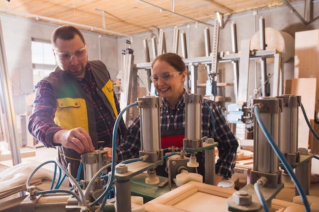 Erfahrener Handwerker, der weiblichen Auszubildenden beibringt, mit Holzbearbeitungsmaschinen zu arbeiten