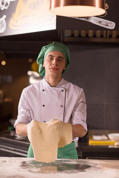 Erfahrener Koch, der Teig zum Pizzarollen mit den Händen zubereitet und sich übergeben kann