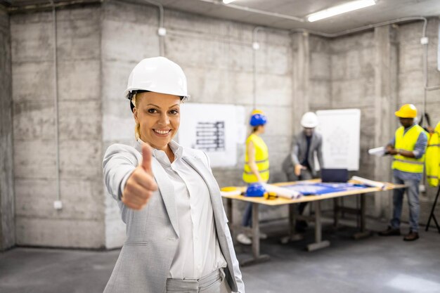 Erfolgreiche Architektin im Business-Anzug und Schutzhelm hält Daumen hoch auf der Baustelle