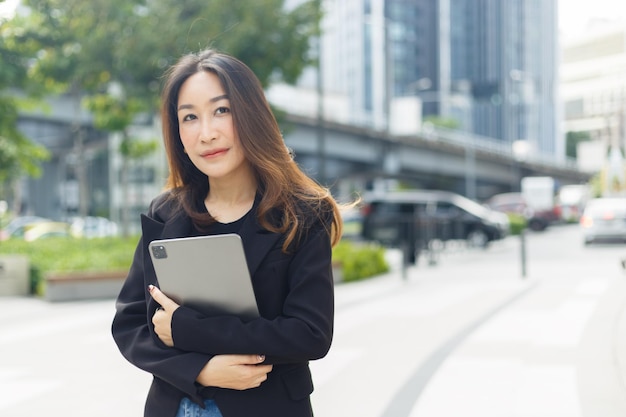Erfolgreiche asiatische Geschäftsfrau trägt einen schwarzen Anzug, der eine Tablette auf der Stadtstraße hält. frau freiberufler lebensstil mensch urban. Kopieren Sie den Speicherplatz für das Textwort.