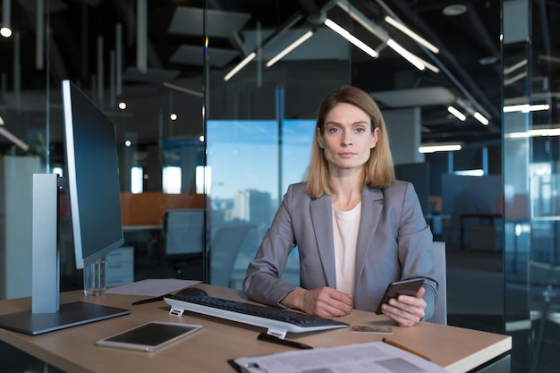 Erfolgreiche Frau, die in einem modernen Büro an einer Computergeschäftsfrau arbeitet, nutzt das Online-Browsing in den sozialen Netzwerken des Telefons