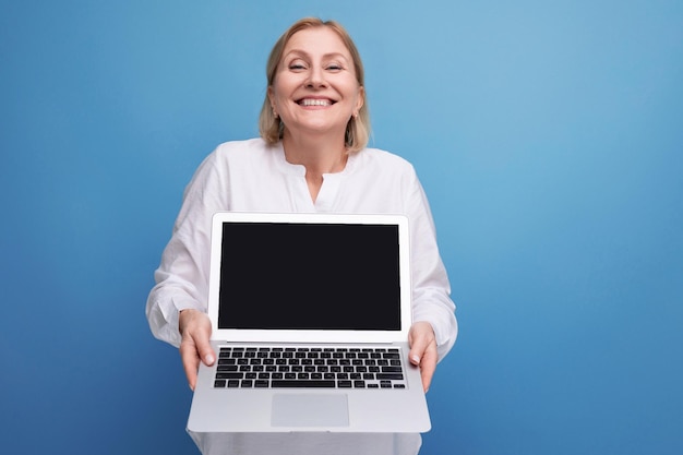 Erfolgreiche Frau mittleren Alters mit blonden Haaren demonstriert einen Laptop mit Mocup