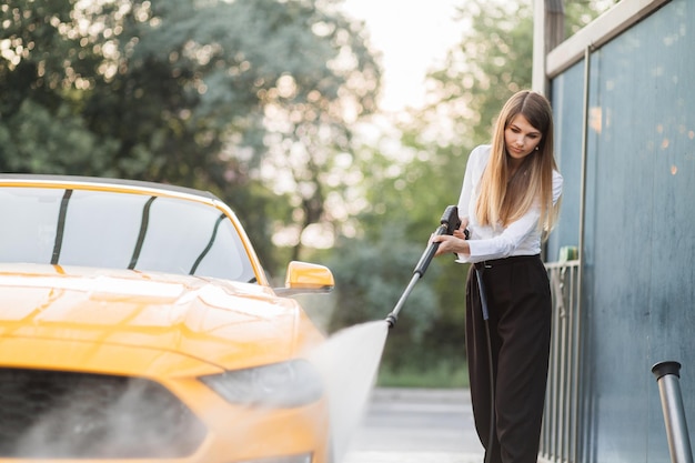 Erfolgreiche Geschäftsfrau, die ein weißes Hemd und eine schwarze Hose trägt und ihr gelbes Auto wäscht