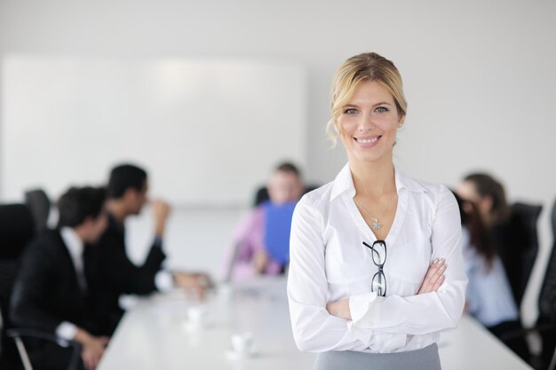Erfolgreiche Geschäftsfrau, die mit ihren Mitarbeitern im Hintergrund in einem modernen, hellen Büro steht