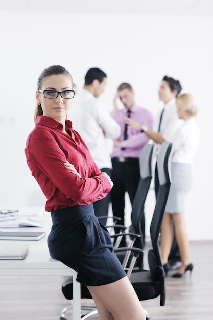 Erfolgreiche Geschäftsfrau, die mit ihren Mitarbeitern im Hintergrund in einem modernen, hellen Büro steht