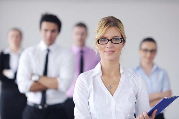 Erfolgreiche Geschäftsfrau, die mit ihren Mitarbeitern im Hintergrund in einem modernen, hellen Büro steht