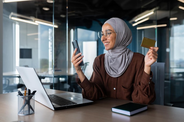 Erfolgreiche Geschäftsfrau im Hijab, die im Büro mit Laptop am Arbeitsplatz arbeitet, muslimische Frau