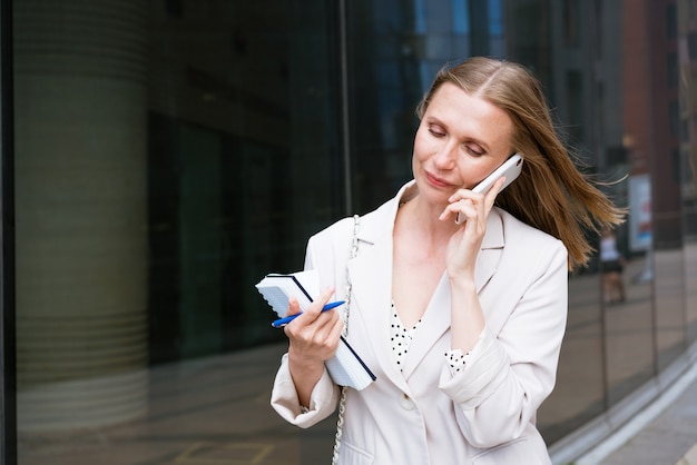 Erfolgreiche Geschäftsfrau oder Geschäftsfrau, die Notizen macht und beim Gehen über das Handy telefoniert...