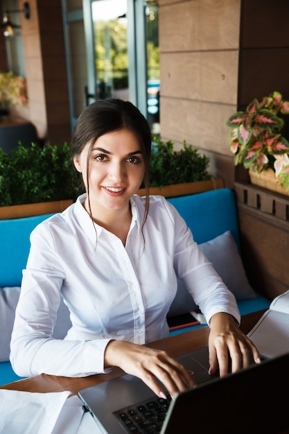 Erfolgreiche glückliche junge Frau, die am Laptop im Café im Freien arbeitet. Porträt der lächelnden Geschäftsfrau