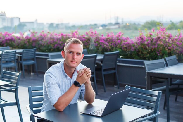 Erfolgreiche junge Führungskraft, die mit einem Laptop auf einer Hotelterrasse an einem Tisch sitzt und im Urlaub in einem exotischen Resort Zeit für die Fernsteuerung von Mitarbeitern findet