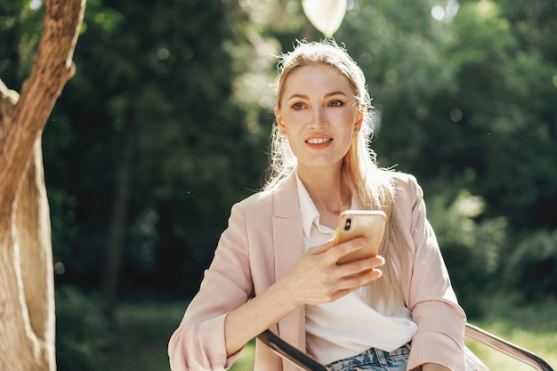 Erfolgreiche junge Geschäftsfrau, die im Café im Freien sitzt und Smartphone benutzt