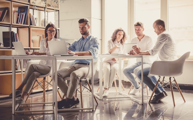 Erfolgreiche junge Geschäftsleute verwenden Gadgets und diskutieren Ideen, während sie im Büro arbeiten