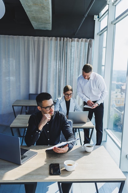 Erfolgreiche Menschen mit Brille sitzen mit einem Laptop an einem Holztisch und arbeiten in einem modernen Büro