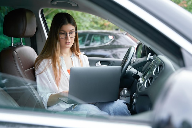 Erfolgreiche, selbstbewusste Geschäftsfrau, die mit einem Laptop auf dem Fahrersitz des Autos sitzt