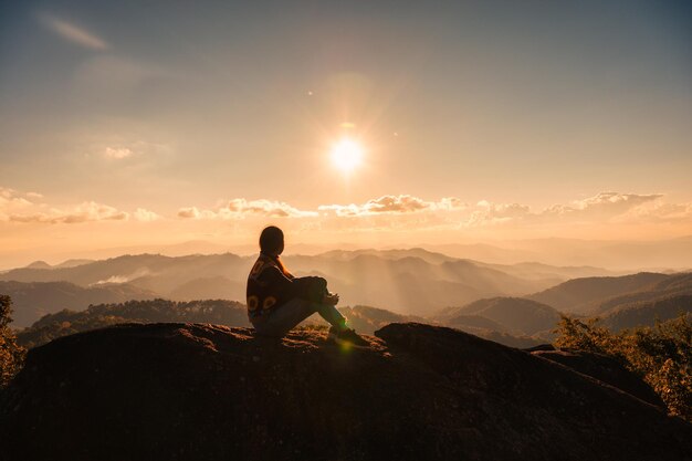 Erfolgreiche Silhouette junge Wanderin, die sich entspannt und den Blick auf den Sonnenuntergang auf dem Gipfel des Nationalparks genießt