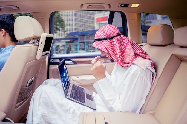 Erfolgreicher arabischer Mann mit Laptop-Computer im Auto