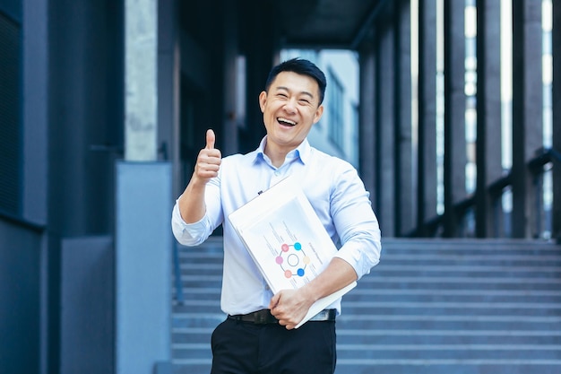 Erfolgreicher asiatischer Geschäftsmann außerhalb des Büros lächelt positiv