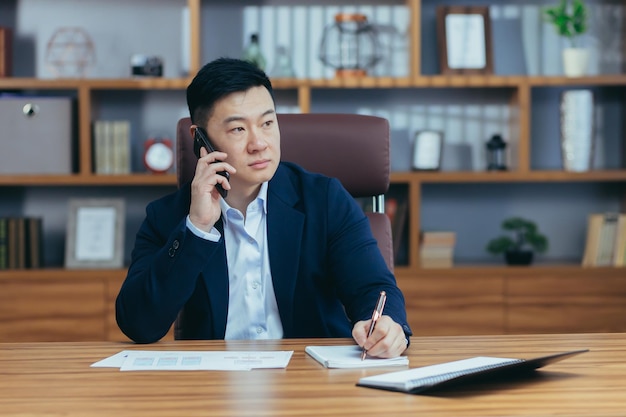 Erfolgreicher asiatischer Geschäftsmann, der in den Bürounterlagen arbeitet und am Telefon spricht