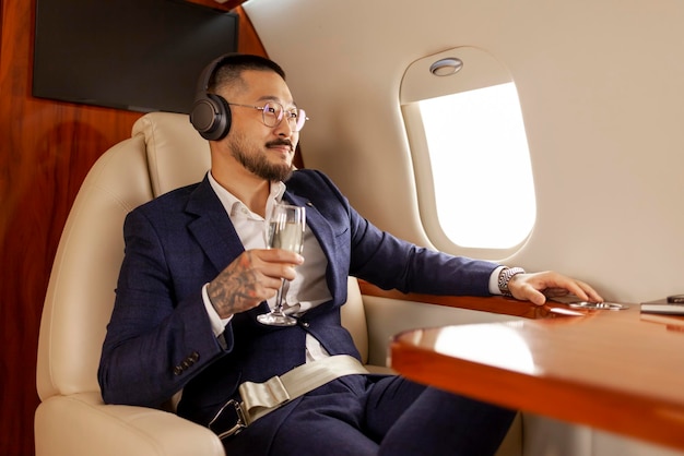 Erfolgreicher asiatischer Geschäftsmann fliegt im privaten Luxusjet mit einem Glas Champagner und hört Musik