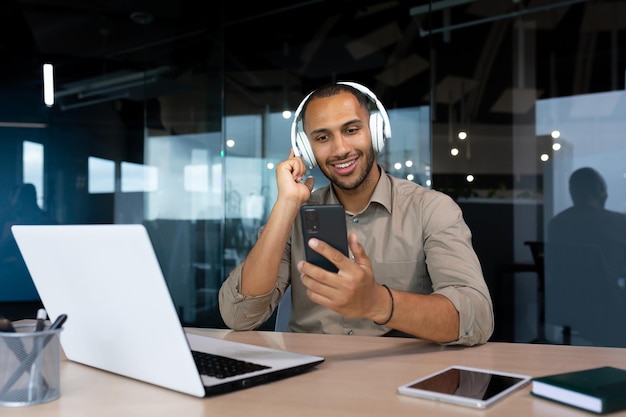 Erfolgreicher Geschäftsmann am Arbeitsplatz mit Telefon, um Online-Videos anzusehen und Musik zu hören und