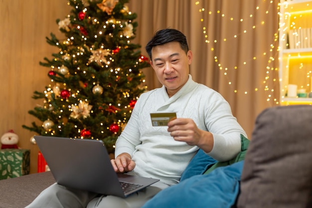 Erfolgreicher Geschäftsmann an Weihnachten zu Hause sitzend auf Sofa im Wohnzimmer mit Laptop online