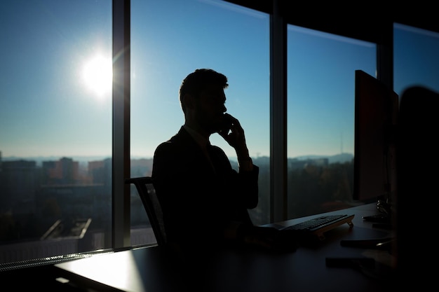 Erfolgreicher Geschäftsmann, der am Computer auf dem Hintergrund einer großen Fenstersilhouette arbeitet