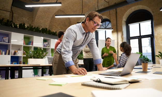 Erfolgreicher Geschäftsmann, der im modernen Coworking Space steht und auf den Laptop-Bildschirm schaut und denkt