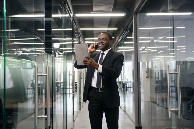 Erfolgreicher Geschäftsmann hat Telefongespräch, während er im leeren Bürokorridor steht. Männlicher professioneller Bankier im Anzug, der während der Arbeitspause auf Mobiltelefon spricht.