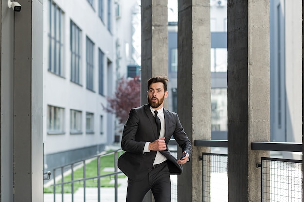 Erfolgreicher Geschäftsmann mit Bart im Business-Anzug rennt in Eile zu einem Treffen in der Nähe des Büros auf der Treppe