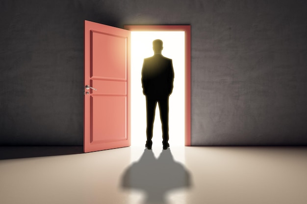 Erfolgreicher Geschäftsmann steht vor einer hellen Tür in einem Betoninnenraum mit Schatten auf dem Boden. Zukünftiger Erfolg und Traumkonzept