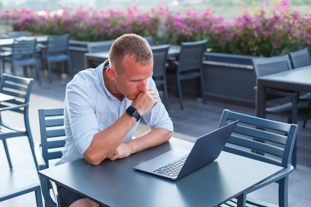 Erfolgreicher junger männlicher Geschäftsmann, der im Urlaub mit Laptop arbeitet. Er trägt ein Hemd und weiße Shorts. Außerhalb des Büros arbeiten, Freiberufler