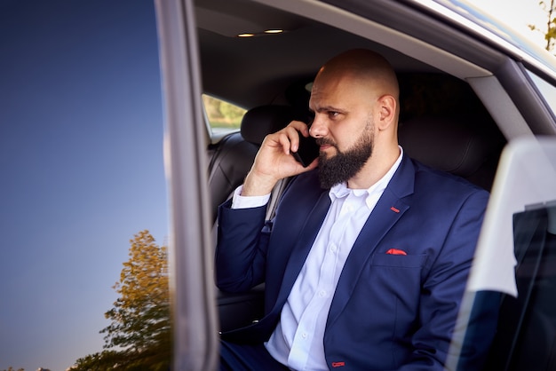 Erfolgreicher junger Mann, der am Telefon in einem Auto spricht.