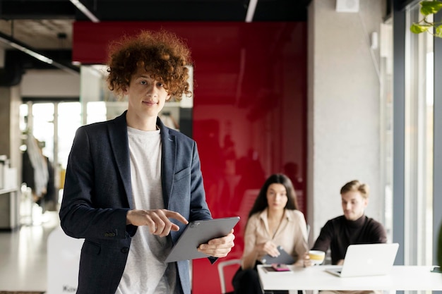 Erfolgreicher junger Mann, der im modernen Büro steht und Tablet in seinen Händen hält Attraktiver Geschäftsmann