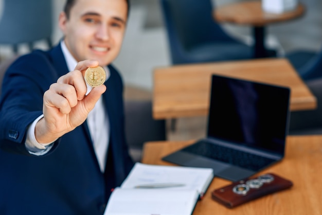 Erfolgreicher lächelnder Geschäftsmann hält eine goldene Bitcoin-Münze in der Hand