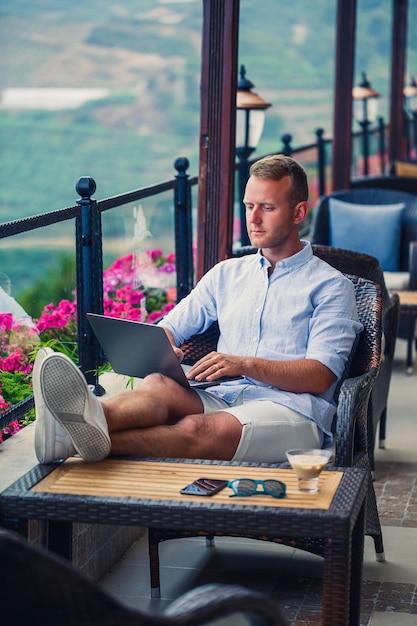 Erfolgreicher männlicher Geschäftsmann, der im Urlaub hinter einem Laptop mit Blick auf die Berge arbeitet Online-Manager-Workflow Arbeiten Sie im Freien mit einer schönen Aussicht vom Balkon