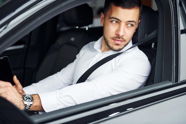 Erfolgreicher Mann Der junge Mann im weißen Hemd sitzt in einem modernen neuen Automobil