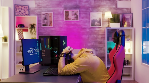 Erfolgreicher Mann, der Online-Videospiele auf seinem Computer spielt. Professioneller Spielspieler in seinem Zimmer mit Neonlichtern.