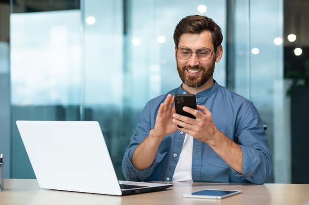 Erfolgreicher und glücklicher Geschäftsmann mit Bart arbeitet in einem modernen, hellen Büro. Männlicher Chef verwendet Laptop