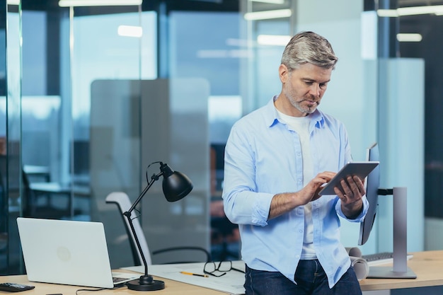 Erfolgreicher und nachdenklicher Geschäftsinhaber verwendet einen Tablet-Computer-Geschäftsmann, der in einem modernen Büro arbeitet