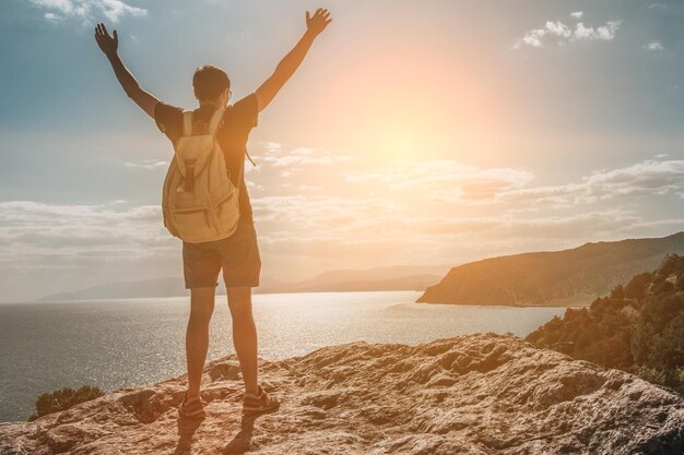 Erfolgskonzept Wanderer mit Rucksack, der mit erhobenen Händen auf einem Berg steht und die Aussicht genießt