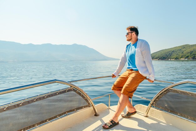 Erfolgsmann, der an der Nase des Bootes steht, mit Meer und Bergen im Hintergrund