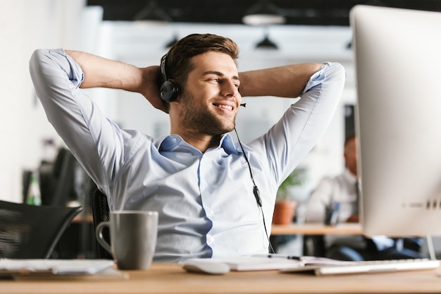 Erfreulicher Büroleiter, der per Headset mit Mikrofon spricht und wegschaut, während er im Büro am Tisch sitzt